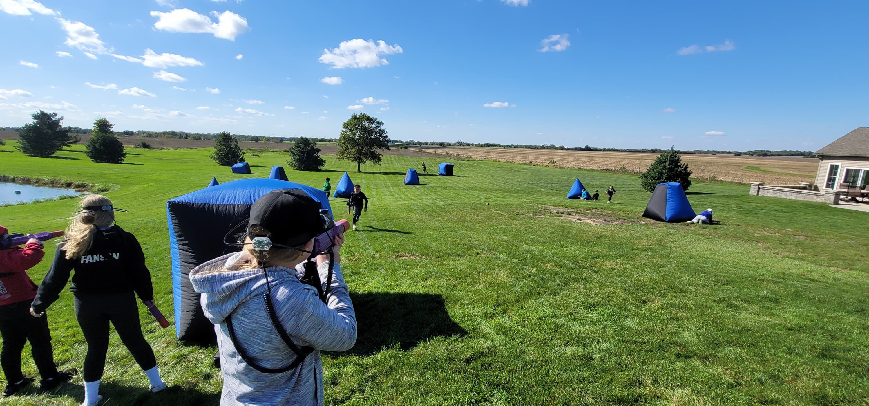 Kids playing laser tag taking aim behind a black and blue obstacle outside on a clear and sunny spring day